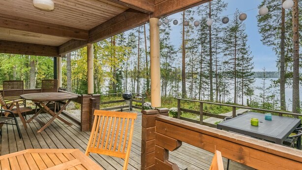 Una terraza de madera con una mesa y sillas, con vista a un lago rodeado de árboles.