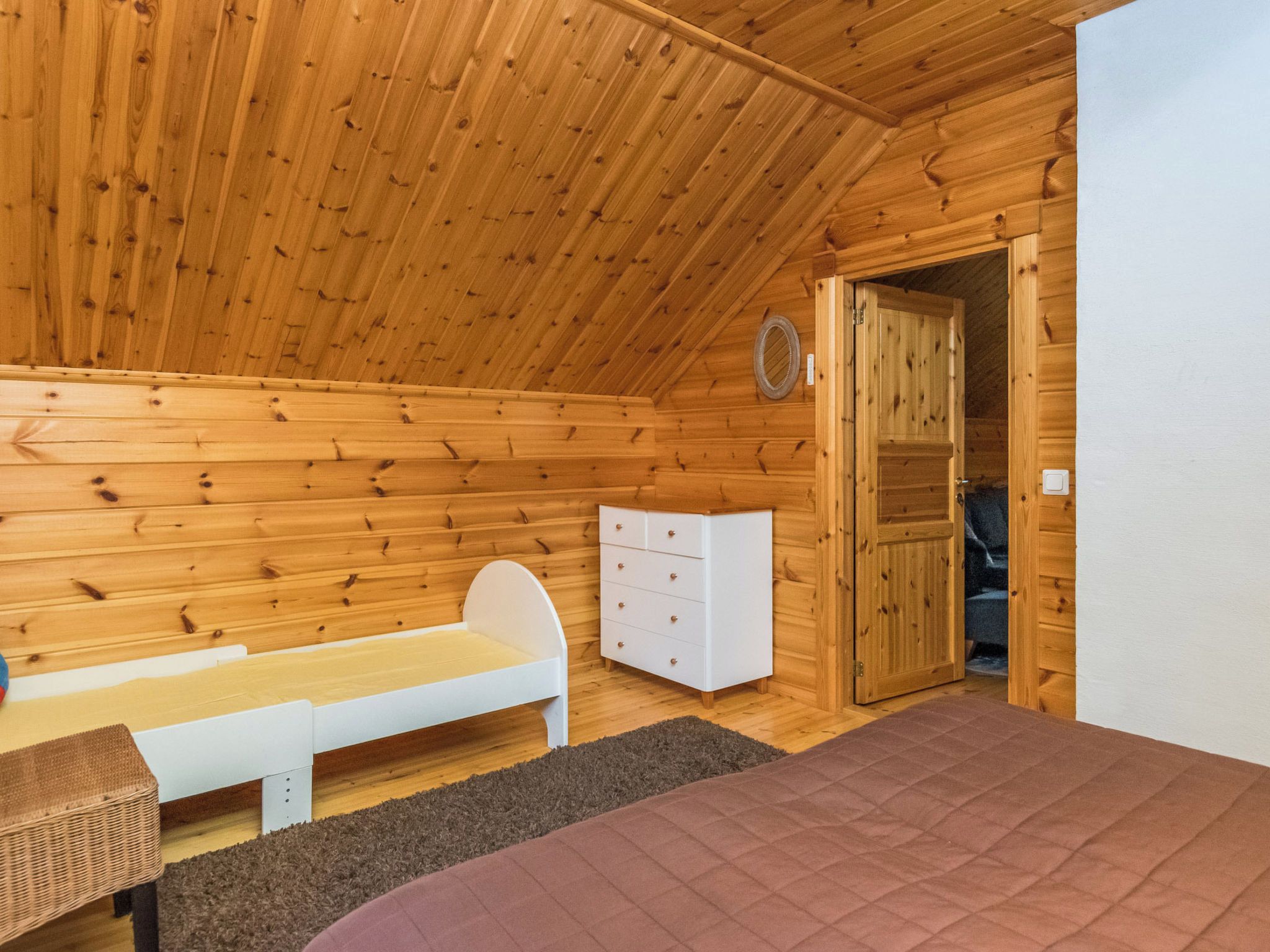 A wooden cabin room with a bunk bed, a white dresser, and a door leading to another room.