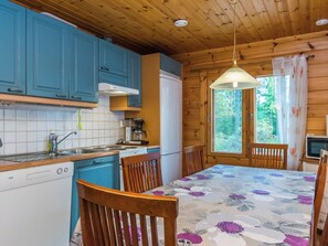 A kitchen with blue cabinets, a white refrigerator, a wooden dining table with floral tablecloth, and wooden chairs. - Metsola / huilinpaikka by Interhome (Kerimäki)