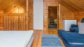 Un dormitorio de cabaña de madera con cama, sofá, cómoda y un baño visible a través de una puerta abierta.