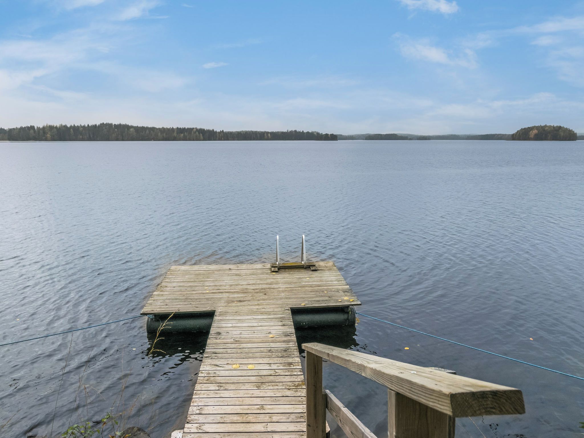 A wooden dock extending into a calm lake with a forested shoreline in the background.