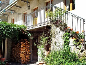 Un bâtiment rustique avec un escalier en pierre, une rampe en métal et une pile de bois de chauffage.