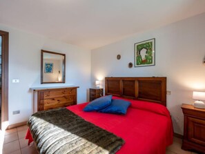 A bedroom with a wooden bed, red bedding, a mirror, a dresser, and a painting on the wall.