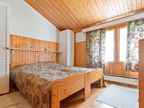 A bedroom with a wooden bed, a headboard, a window with curtains, and a ceiling fan.
