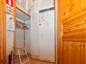 Una habitación pequeña con una puerta de madera, un armario blanco con perchero y un refrigerador blanco.
