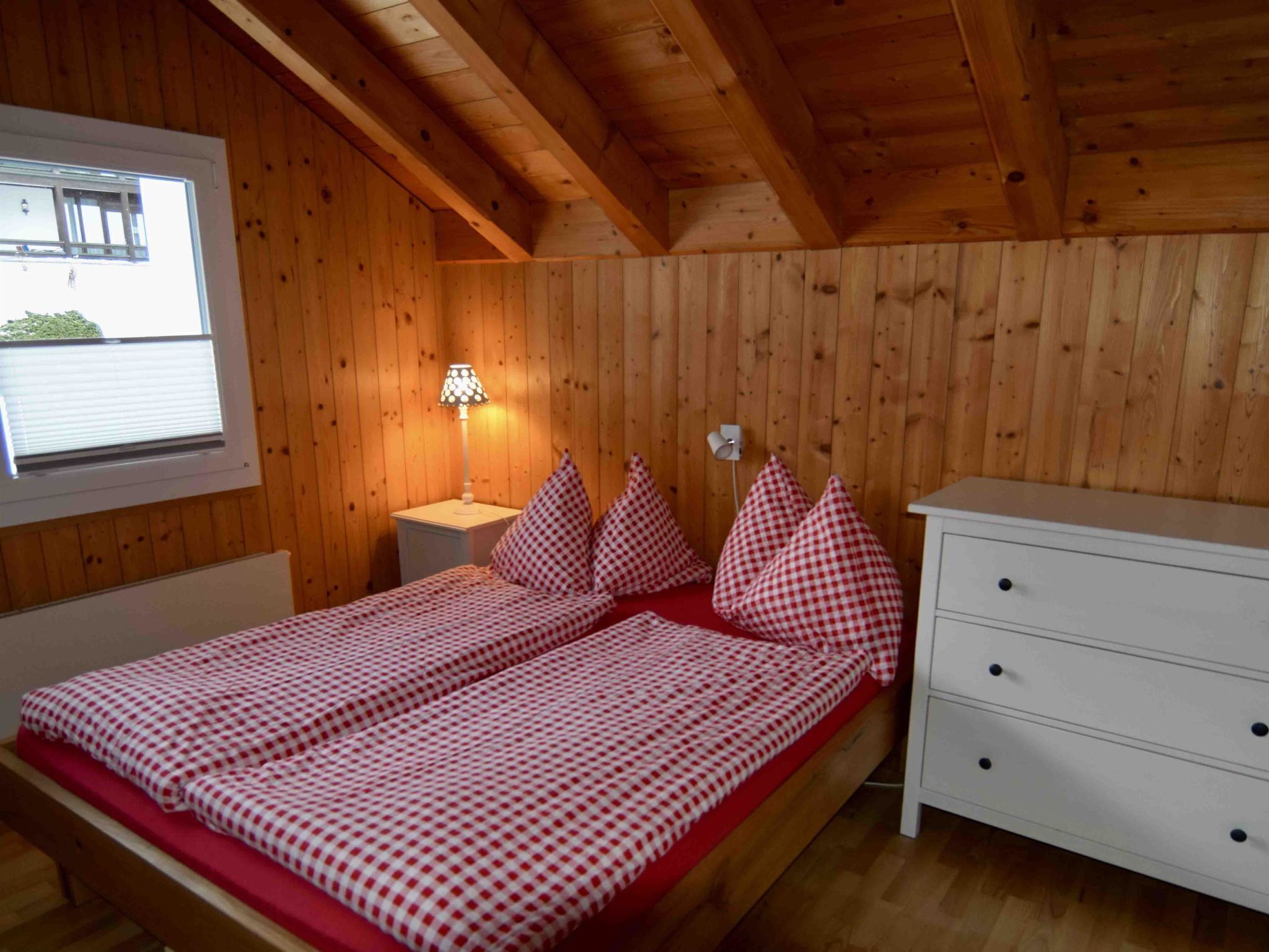 A wooden-paneled room with a bed, a nightstand, a lamp, and a window.