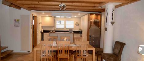 Un comedor con una mesa y sillas de madera, una cocina al fondo y una pared blanca con un letrero.