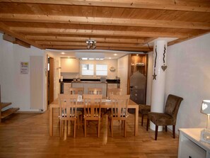 Een eetruimte met een houten tafel en stoelen, een keuken op de achtergrond en een witte muur met een bordje.