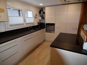 A modern kitchen with white cabinets, a black countertop, and stainless steel appliances. - Bühl 13 Appartement/Fewo 8-Bettwohnung by Interhome (Engelberg)