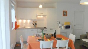 A compact kitchen with white cabinets, a dining table with orange tablecloth, and a microwave on the counter.