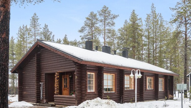 Une cabane en rondins avec un toit enneigé, un porche à l’avant et une cheminée.