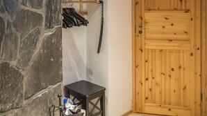 Une pièce avec un mur en pierre, une porte en bois, une petite table avec une poubelle et un portant à vêtements avec des cintres.