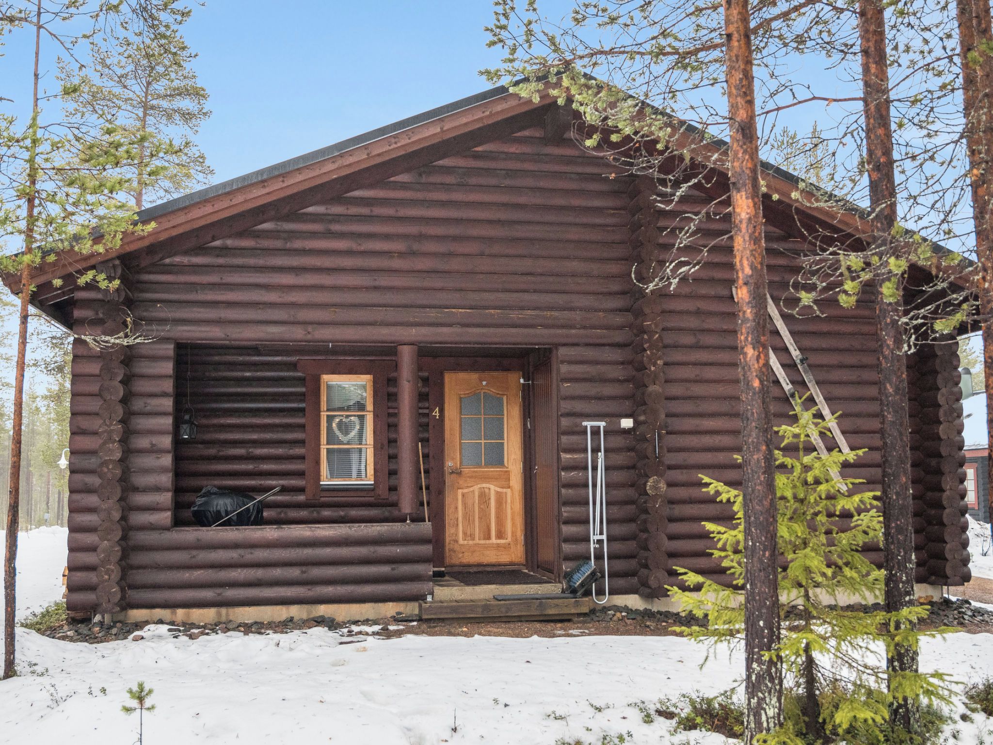 A log cabin with a wooden door and windows, surrounded by snow and trees.