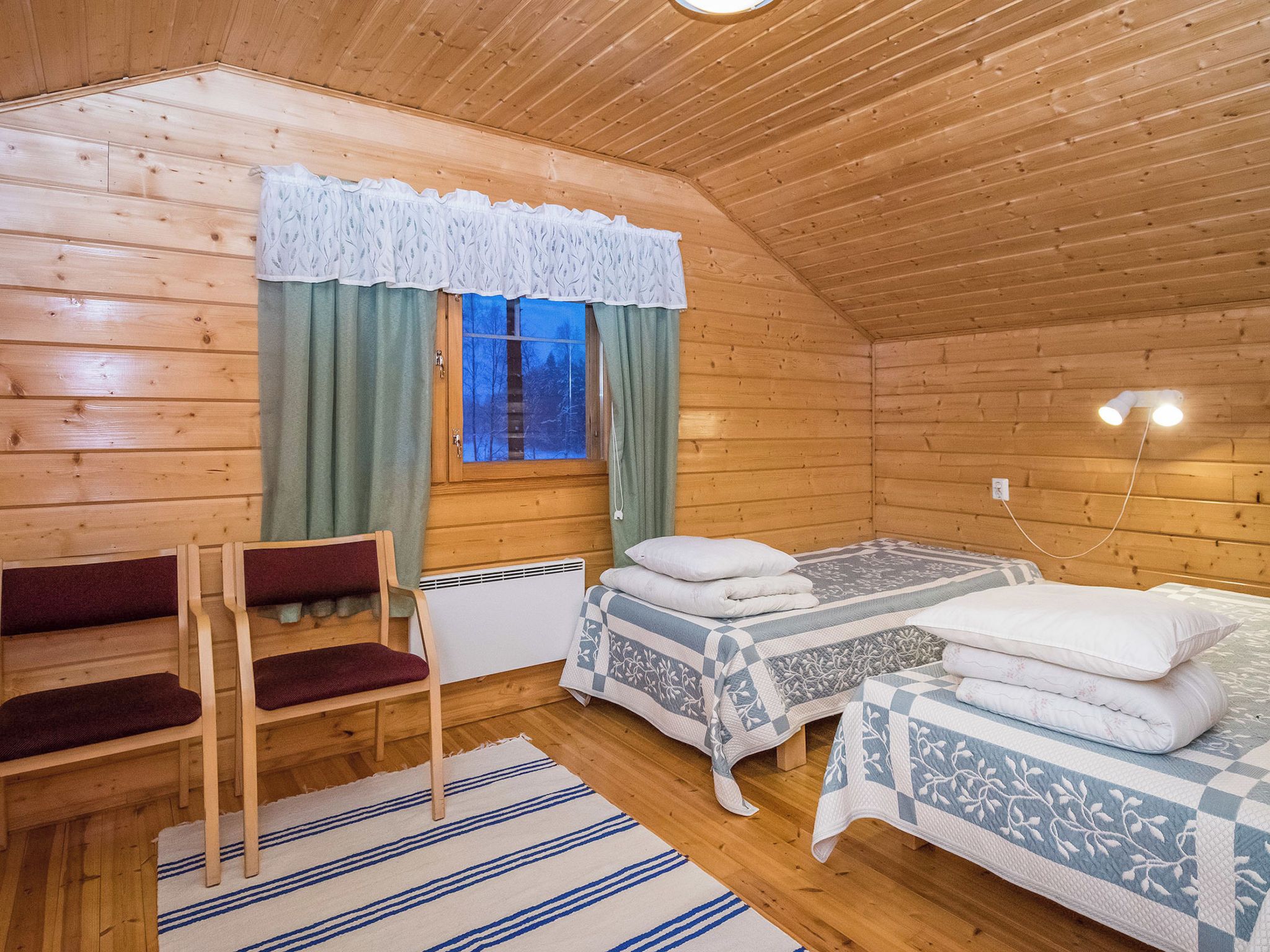 A cozy wooden cabin room with two beds, a bench, and a window with curtains.