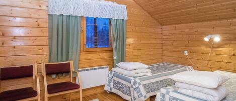 A cozy wooden cabin room with two beds, a bench, and a window with curtains.