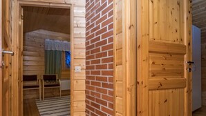 A wooden interior with a brick wall, a door, and a small seating area with a striped rug. - Vaahtera by Interhome (Kaavi)