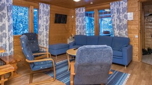 A cozy cabin interior with a blue sofa, a blue armchair, a wooden dining table, and a small TV mounted on the wall. - Vaahtera by Interhome (Kaavi)