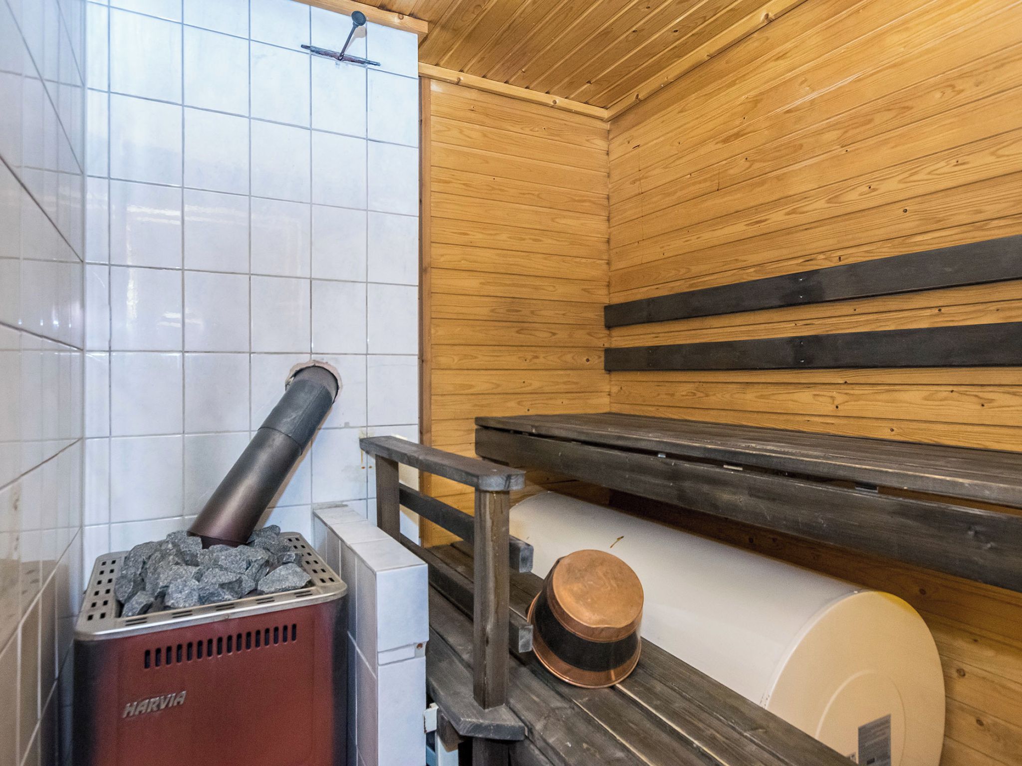 Una sala de sauna con calentador de piedra, banca de madera y un perchero para toallas.
