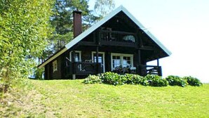 Een houten blokhut met een schuin dak, een schoorsteen en een veranda met treden.