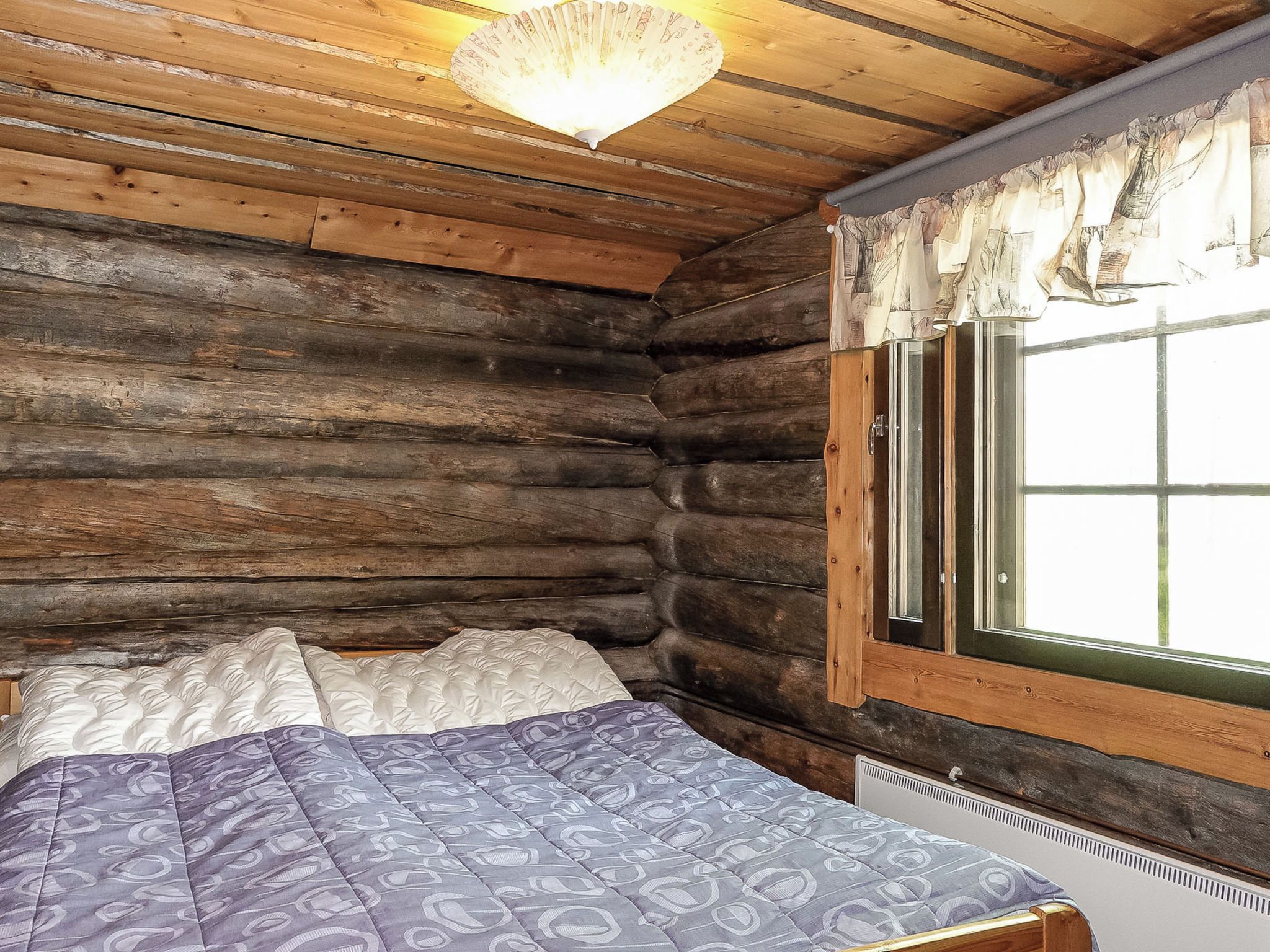 Une chambre de style rustique, avec un lit, une fenêtre avec des rideaux et un luminaire suspendu.