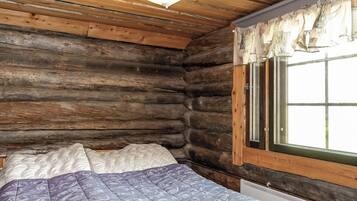 Une chambre de style rustique, avec un lit, une fenêtre avec des rideaux et un luminaire suspendu.