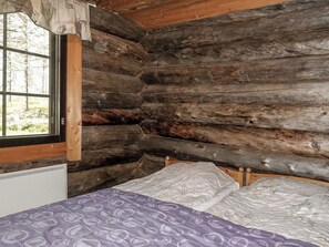 Habitació d'una cabana de fusta amb un llit, una finestra amb cortines i un radiador.