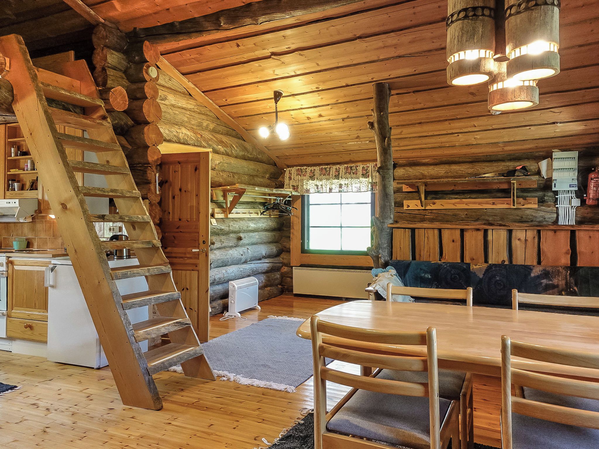 Ein rustikales Holzhaus-Interieur mit einer Holztreppe, einem Esstisch mit Stühlen, einem Fenster mit Vorhängen und einem Kamin.