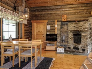 A log cabin interior with a dining area, wooden furniture, a stone fireplace, and a television. - Kulpakko 3 by Interhome (Rovaniemi)