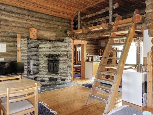 A rustic cabin interior with a stone fireplace, wooden furniture, a television, and a wooden ladder. - Kulpakko 3 by Interhome (Rovaniemi)