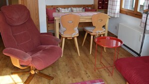 A cozy room with a red armchair, a wooden dining table with two chairs, a small red table, and a radiator. - Elena # 1 by Interhome (Lenk)