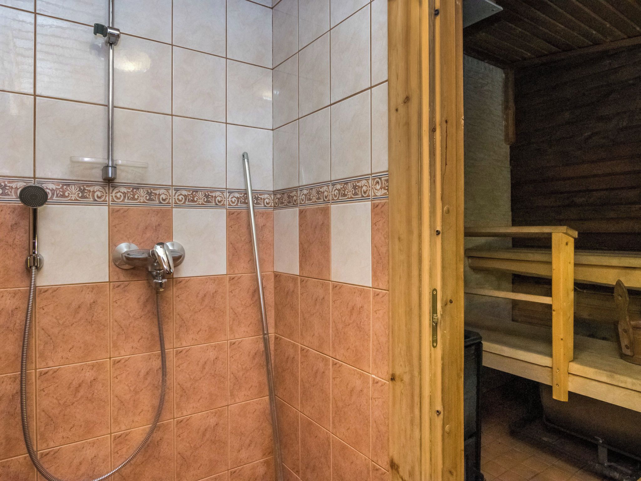 Een douchegedeelte met een betegelde wand, een houten deurkozijn en een metalen douchekop.