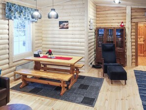 A cozy log cabin interior with a wooden dining table, benches, a black armchair, and a wooden cabinet with glass doors. - Lassinmaja by Interhome (Hartola)