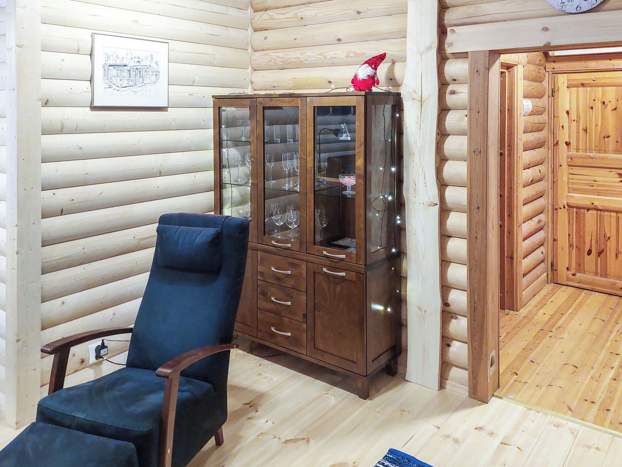 A wooden interior with a glass cabinet displaying wine glasses, a blue chair, and a wooden door.