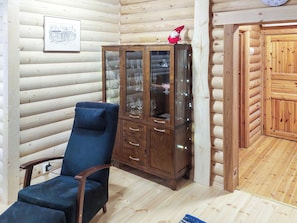 A wooden interior with a glass cabinet displaying wine glasses, a blue chair, and a wooden door. - Lassinmaja by Interhome (Hartola)