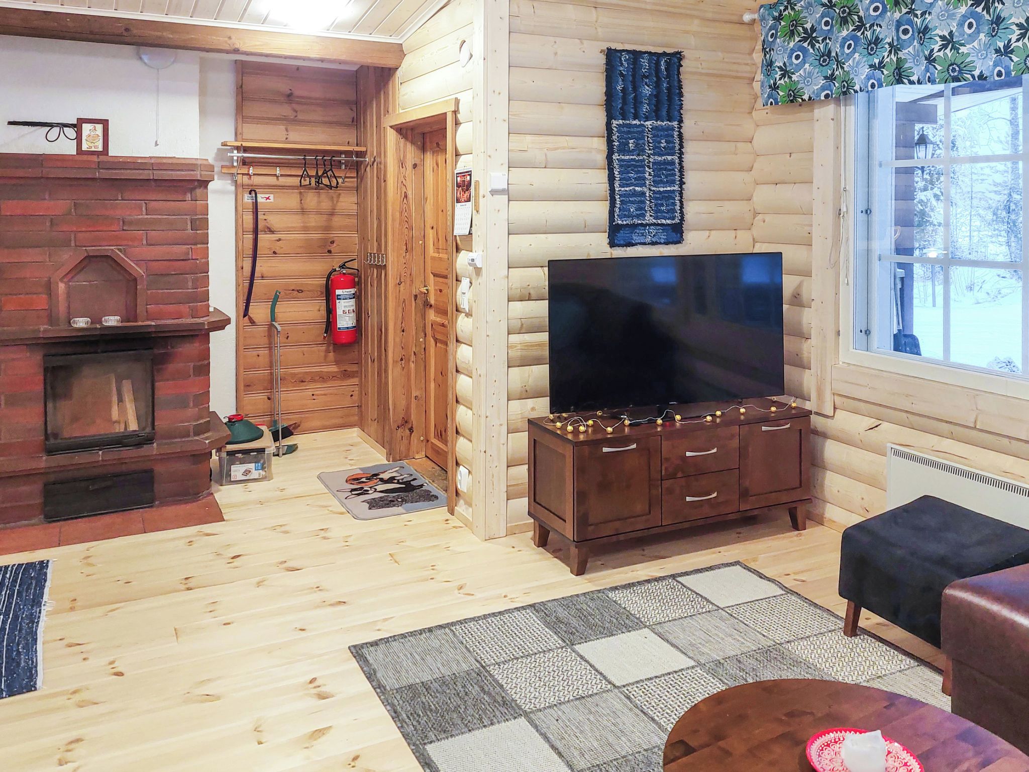 Ein rustikales Blockhaus-Interieur mit Kamin, Fernseher und einem Fenster mit Blick.