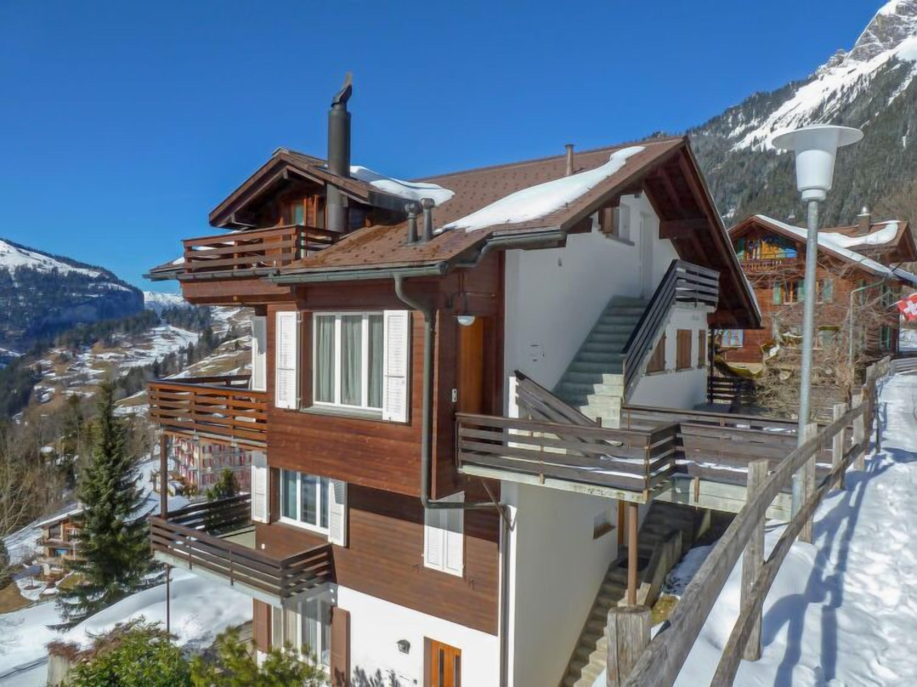 Un moderno chalet con rivestimento in legno, un balcone e una scala che conduce a un piano superiore.