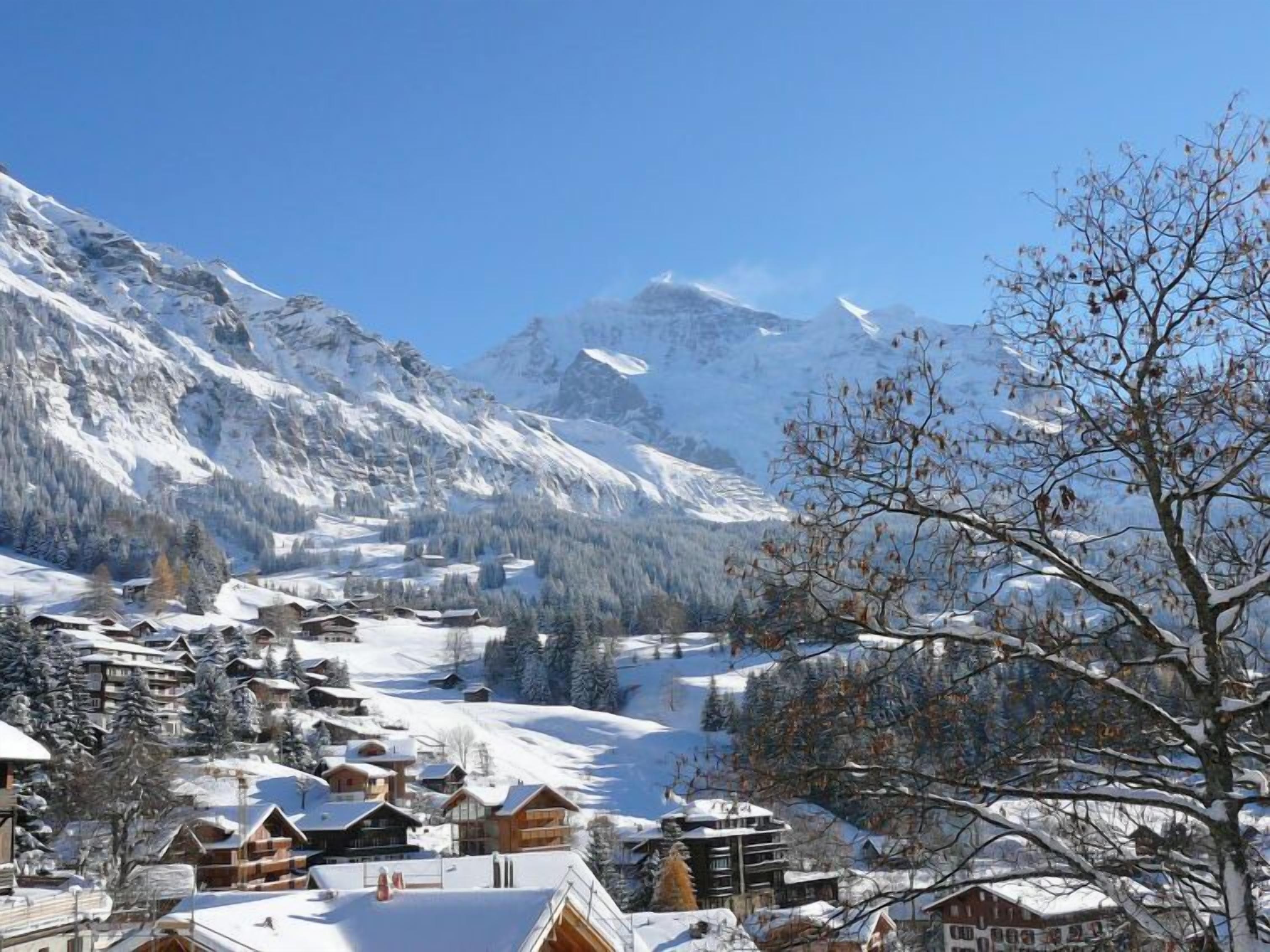 Un village de montagne enneigé, avec des bâtiments en bois et un ciel bleu azur.