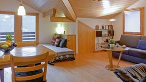 Ein gemütliches Zimmer mit Holzbalkendecke, einem Esstisch mit Stühlen, einer Couch und einem kleinen Beistelltisch.