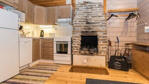 Een keuken met houten kastjes, een stenen openhaard, een witte koelkast en een houten vloer.