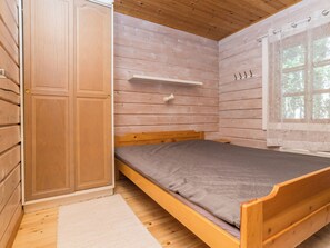 A wooden room with a bed, a wardrobe, a shelf, and a window with a curtain.