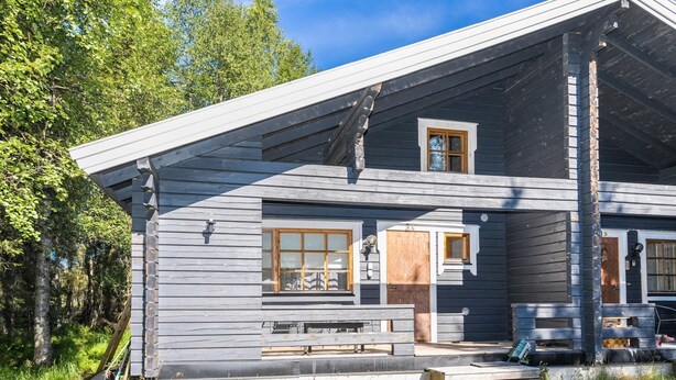 Een chalet met twee verdiepingen, een veranda, grote ramen en een stenen schoorsteen.