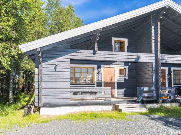 A two-story log cabin with a porch, a small window, and a door.