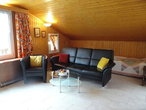 A cozy living room with a black leather sofa, a matching armchair, and a glass coffee table.