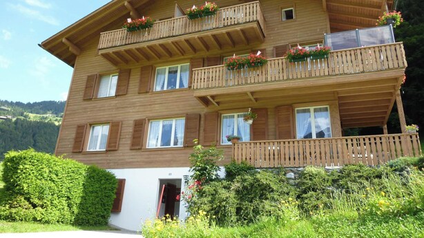 Un immeuble en bois à plusieurs étages, doté de balcons, d’une entrée couverte et d’un espace jardin.
