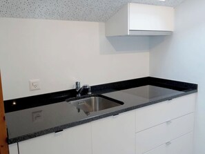 A kitchen with a stainless steel sink, black granite countertop, white cabinets, and a white ceiling with a speckled pattern.