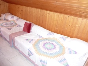 Ein Einzelbett mit gemustertem Bettbezug und einem roten Kissen in einem Zimmer mit Holzwänden.