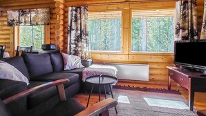 A log cabin interior with a sofa, a small round table, a TV, and large windows with curtains. - Honkala by Interhome (Soini)
