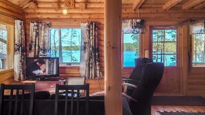 A log cabin interior with a television, wooden furniture, and large windows offering a view of a lake. - Honkala by Interhome (Soini)