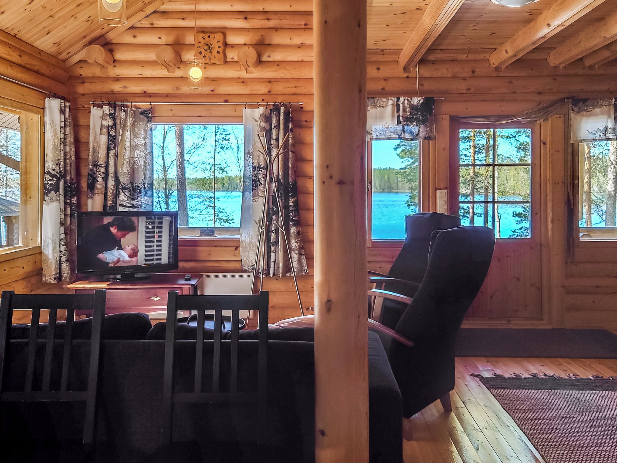 A cabin interior with a television, wooden walls, and a view of a lake.