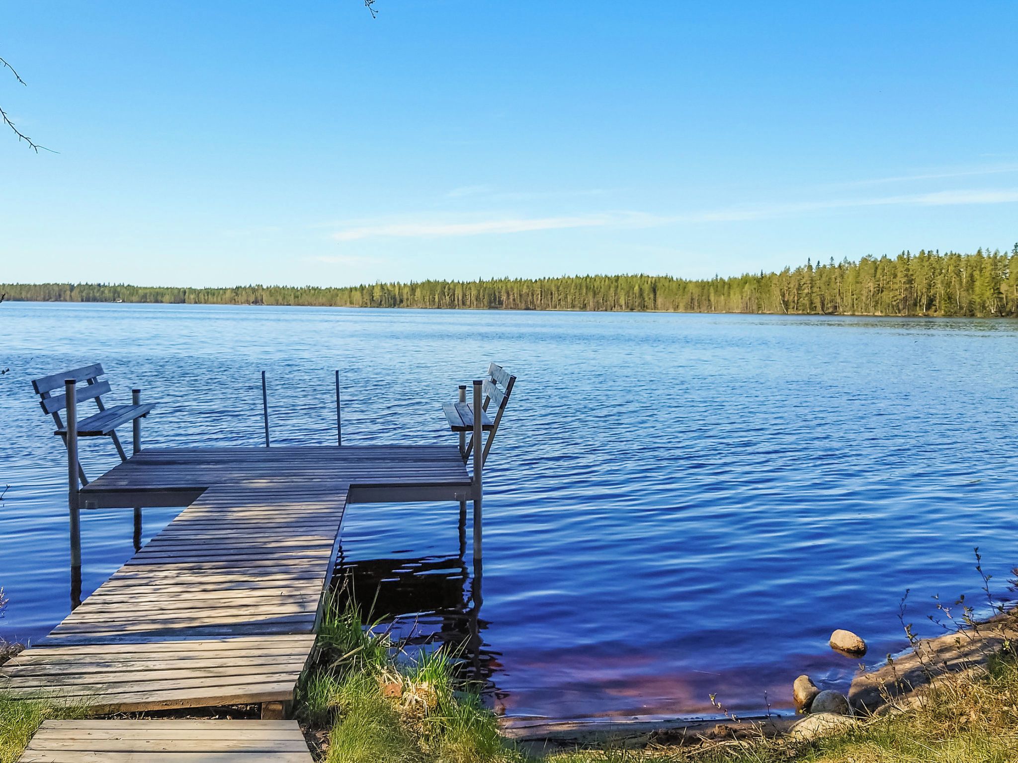 Une jetée en bois s’étendant sur un lac paisible, avec une forêt en arrière-plan.